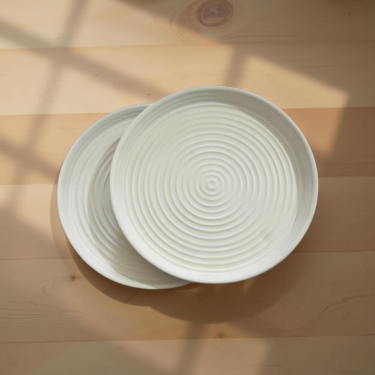 Two white ceramic plates with textured surface on a wooden surface