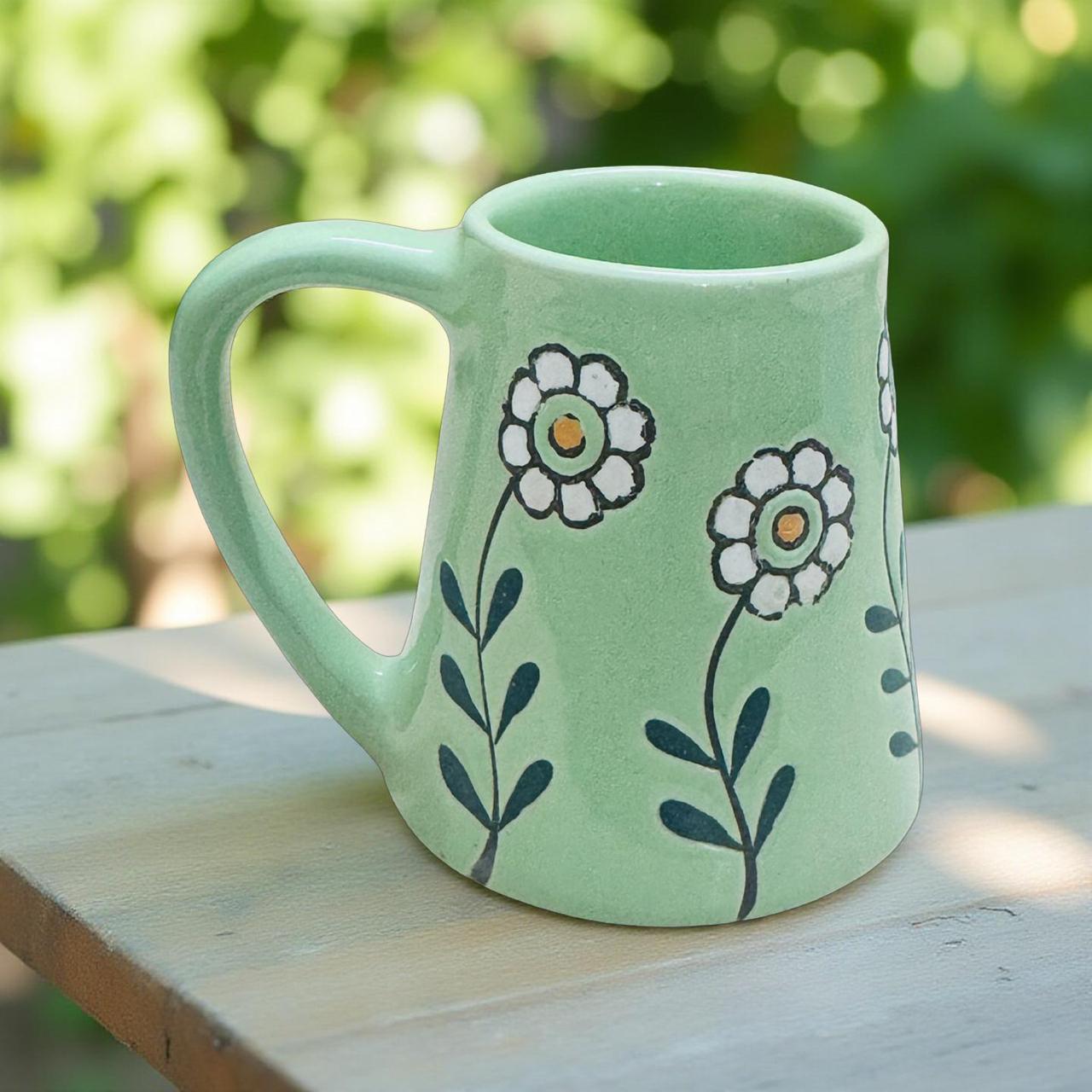Green mug with floral designs on a wooden surface with a blurred natural background