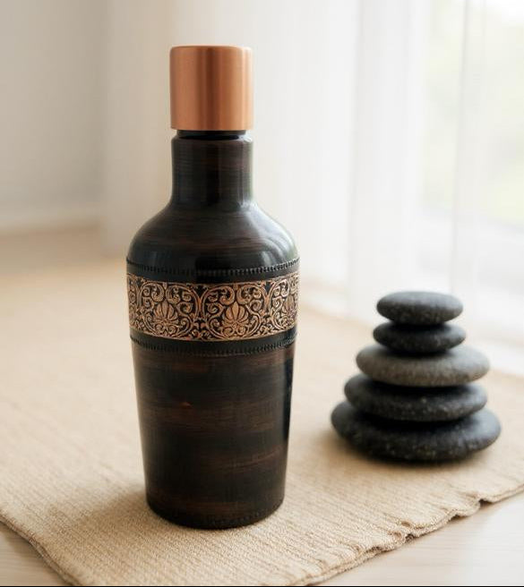 Decorative bottle with a copper cap and intricate design on a textured surface with stacked stones.