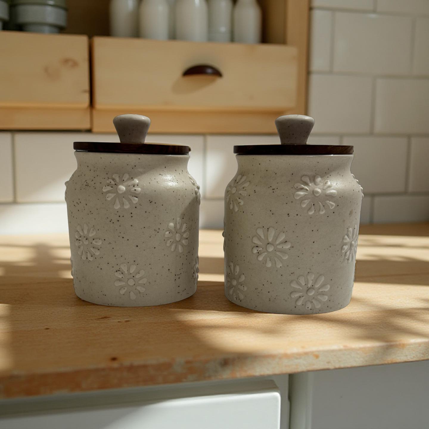 Set of two floral embossed ceramic storage jars with dark wooden lids on a wooden kitchen counter