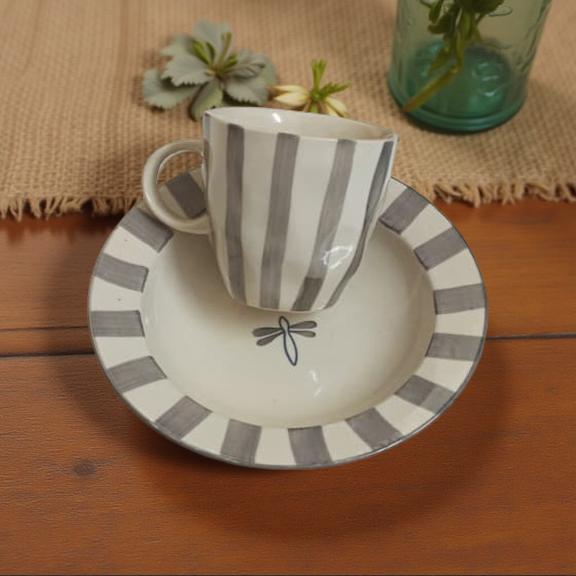 Ceramic cup and saucer with gray stripes on a wooden surface
