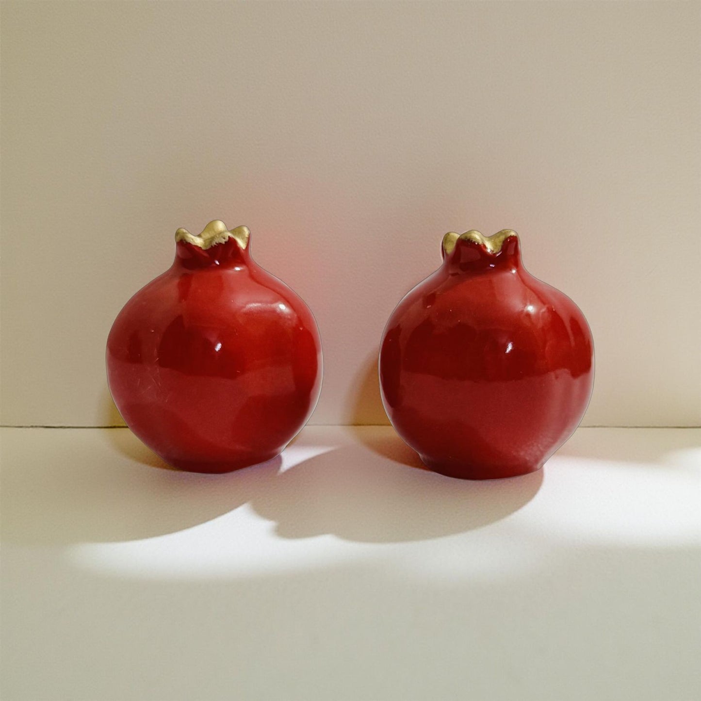 Red ceramic salt and pepper shaker set shaped like pomegranates with golden tops on a marble table