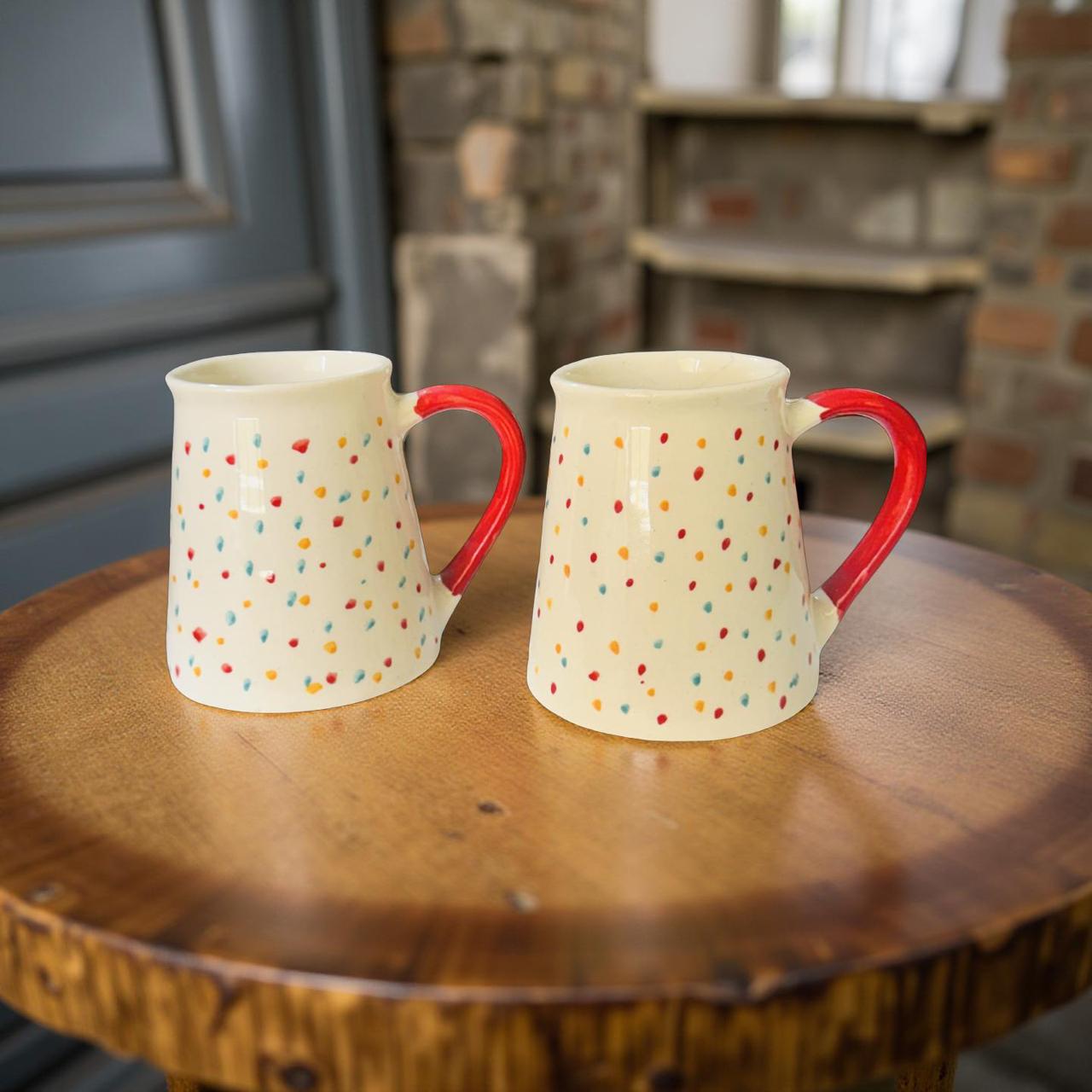 Two ceramic mugs with red handles and multicolored polka dots on a wooden surface.