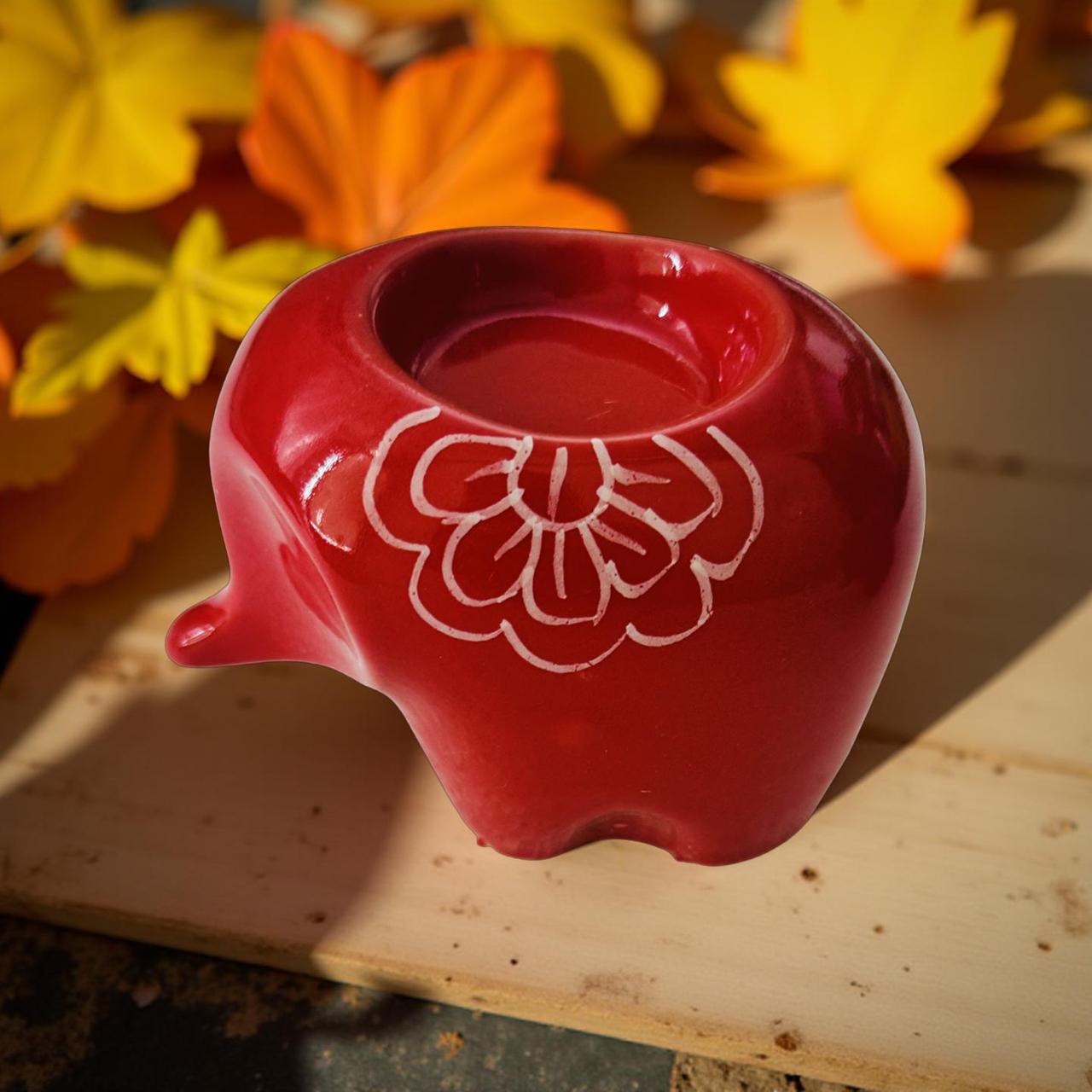 Red ceramic container with floral design on a wooden surface with autumn leaves in the background