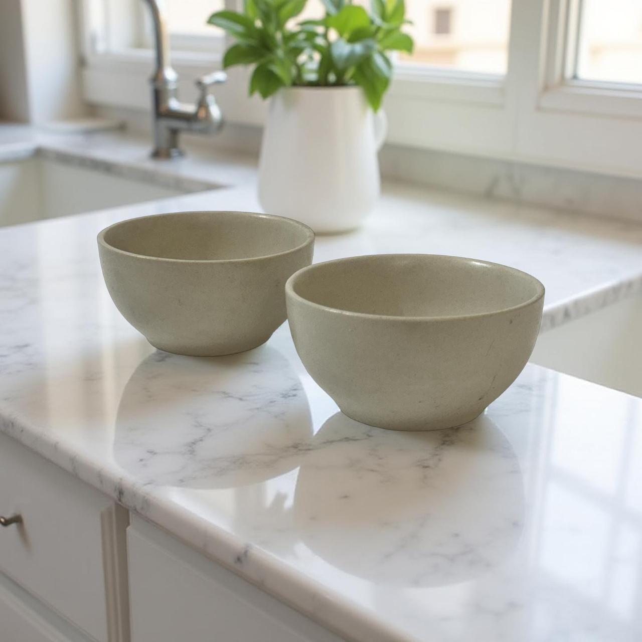 Two beige bowls on a marble countertop with a kitchen background