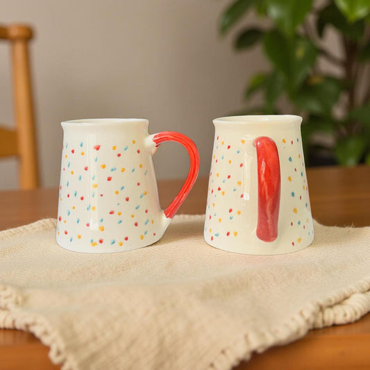 Two ceramic mugs with colorful polka dot patterns on a wooden table.