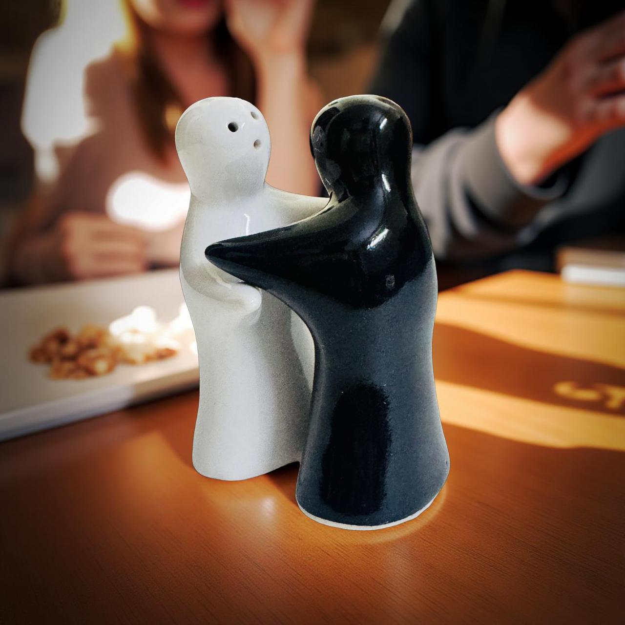 Two ceramic figures, one white and one black, on a table with blurred people in the background.