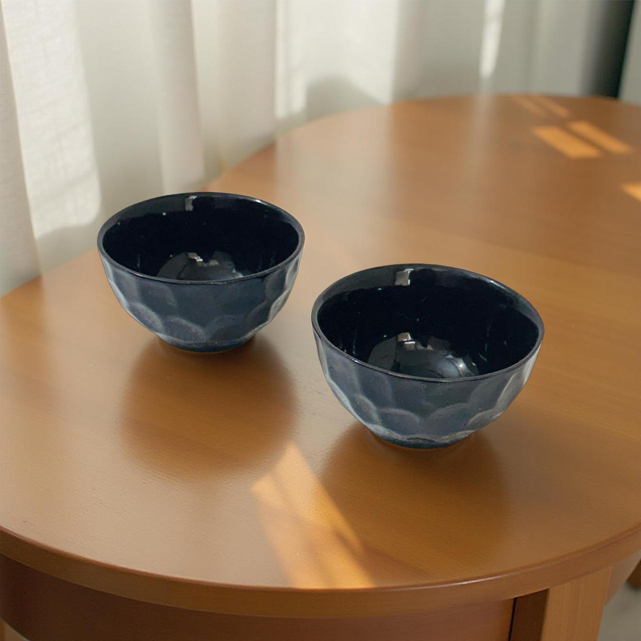 Two black ceramic bowls on a wooden table with a light curtain background