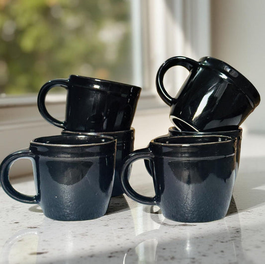 Set of black mugs on a marble surface with a blurred outdoor background