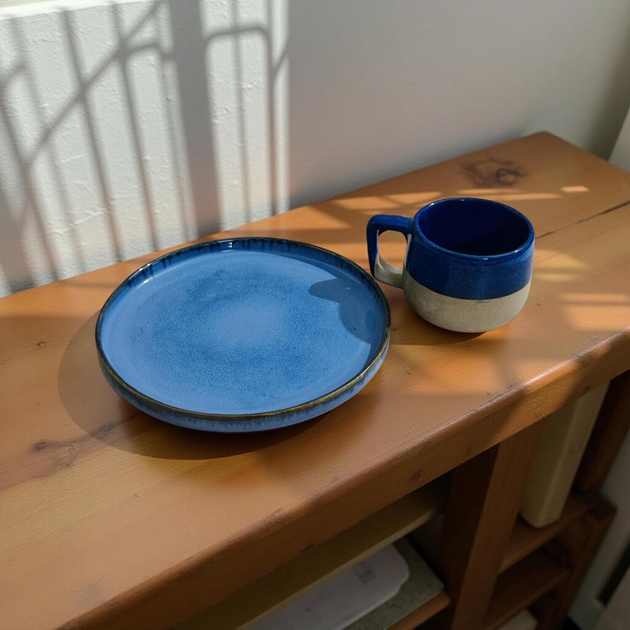 Blue ceramic plate and mug on a wooden surface with sunlight casting shadows.