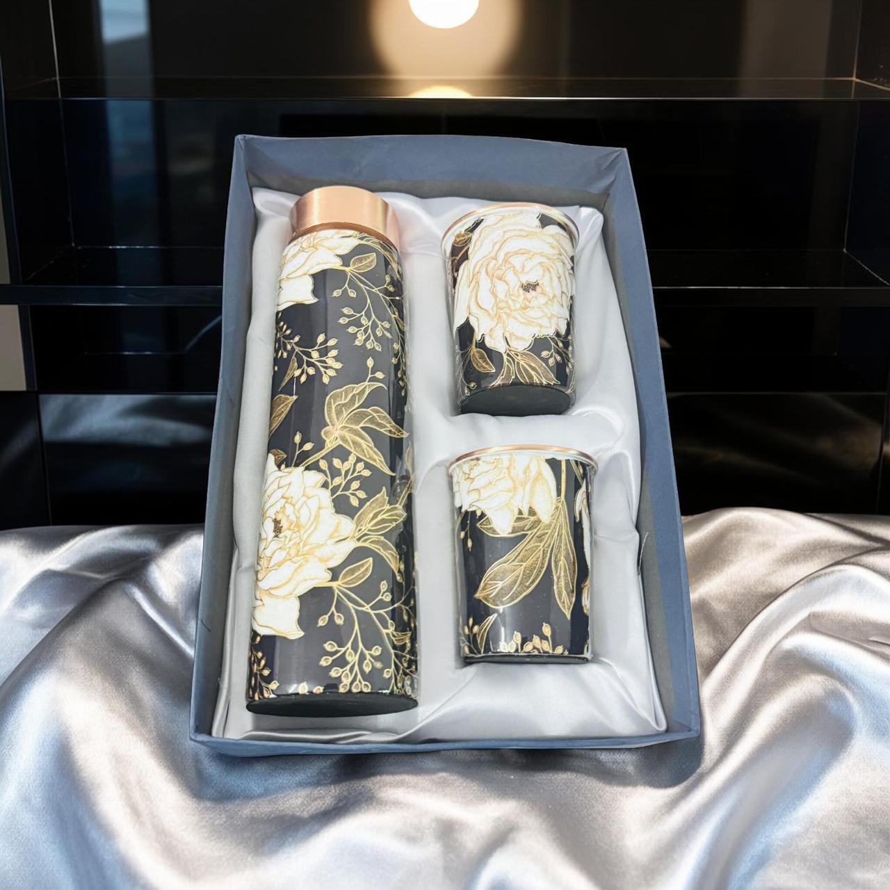 Set of black tumblers with floral designs in a box on a white fabric background