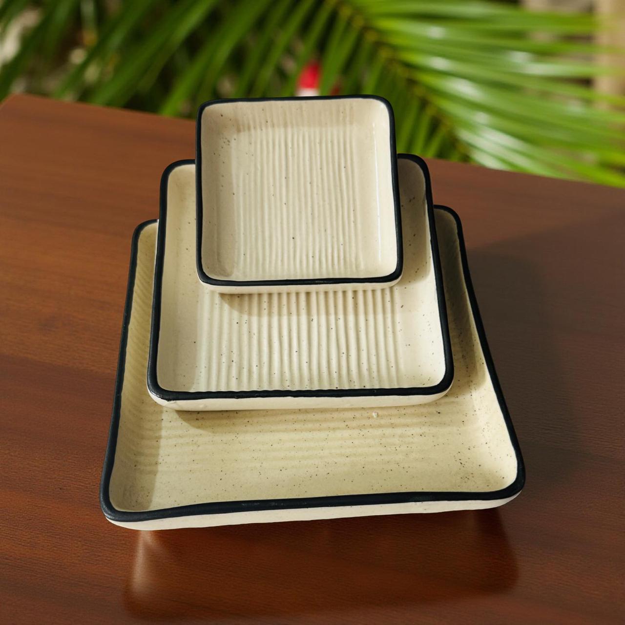 Set of three square ceramic dishes with textured surface on a wooden surface with green foliage in the background