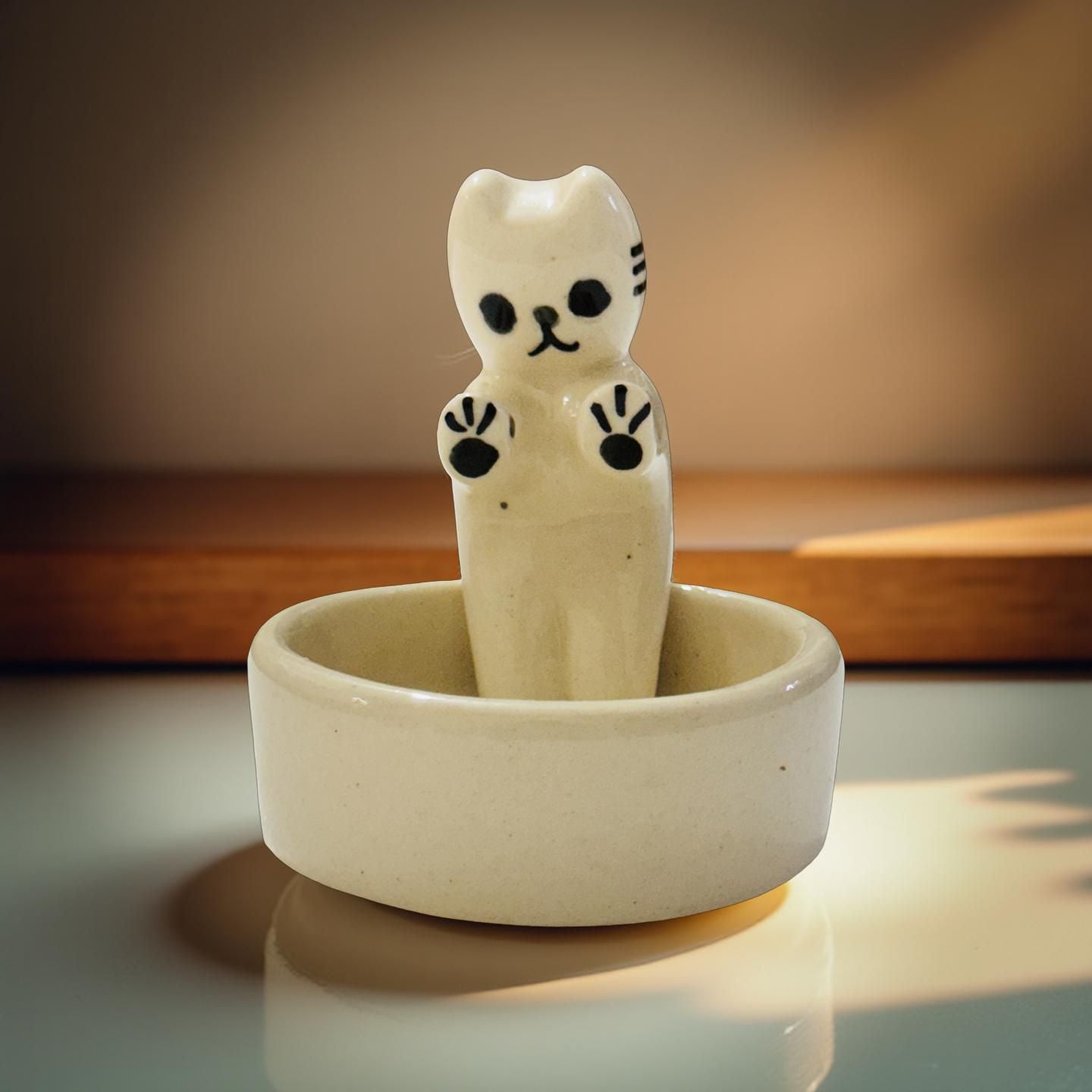 Ceramic cat figurine inside a bowl on a reflective surface with a blurred background