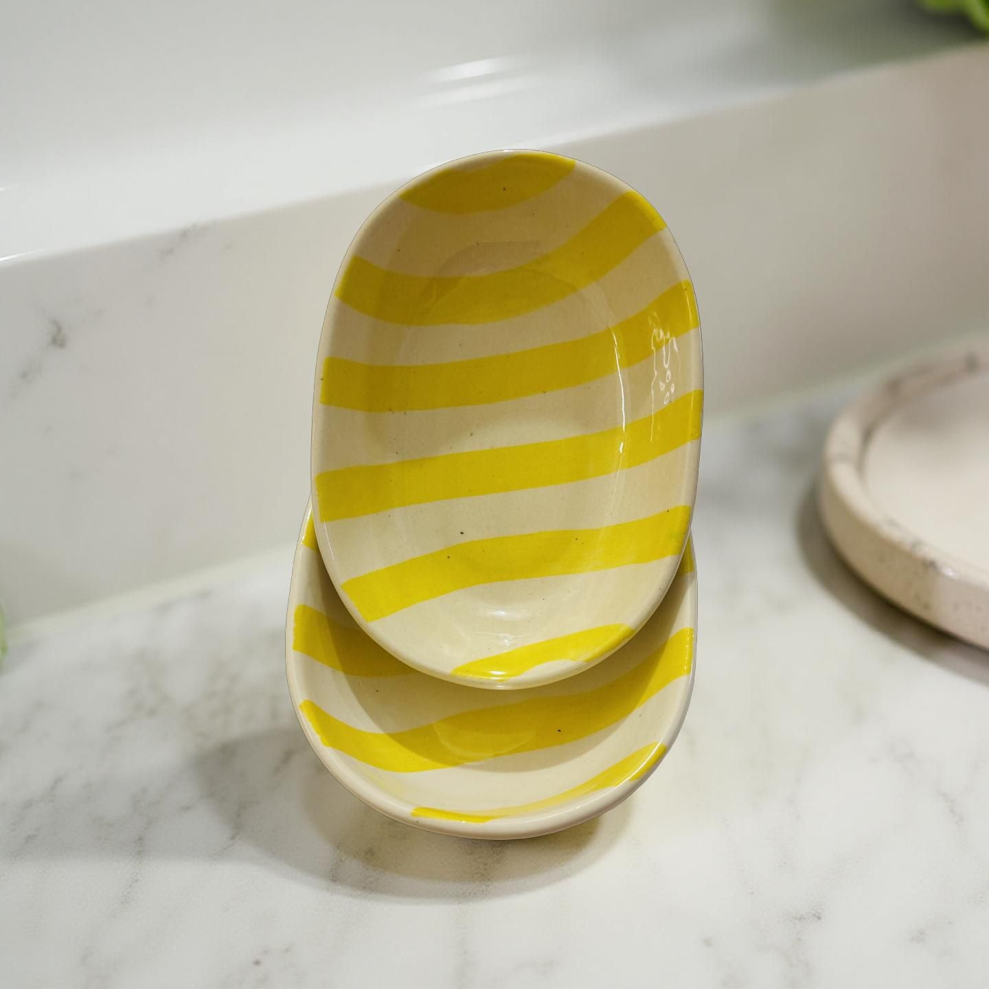 Two ceramic bowls with yellow stripes on a marble surface