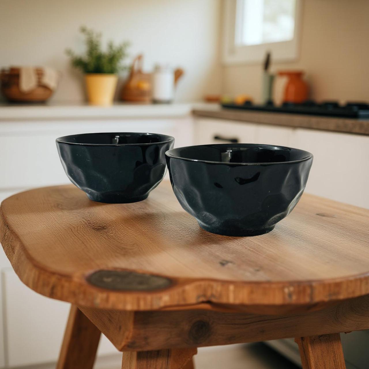 Two black ceramic bowls on a wooden stool in a kitchen setting.