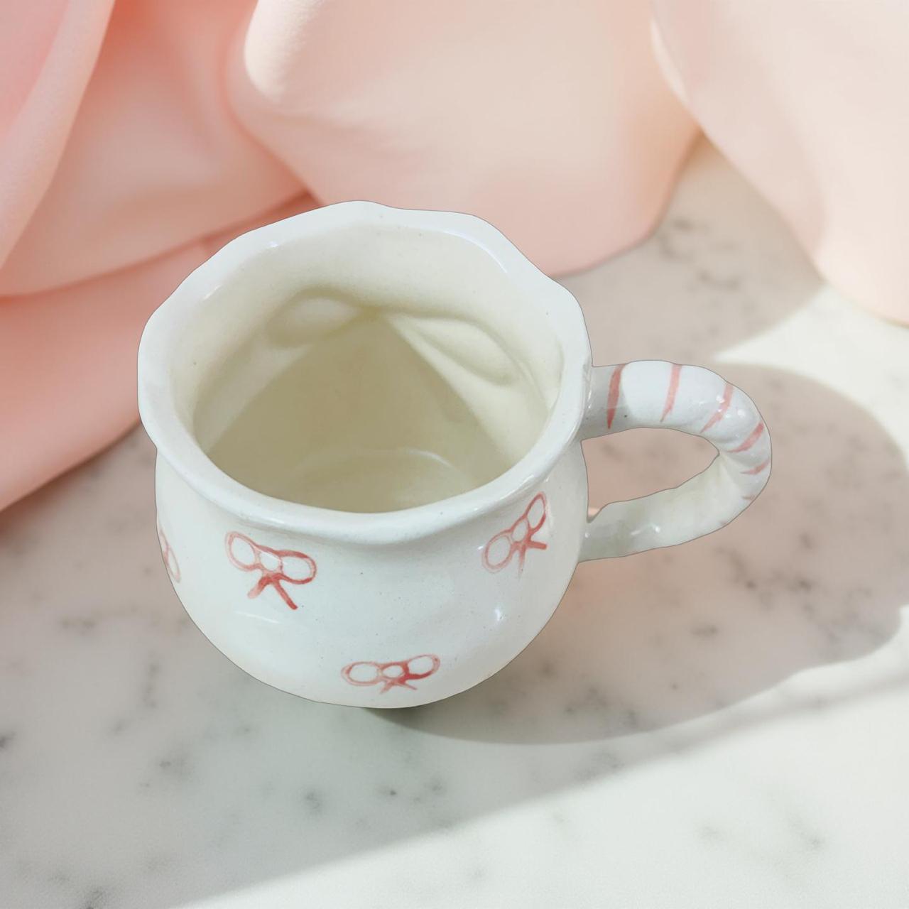 Small white cup with red bow designs on a marble surface