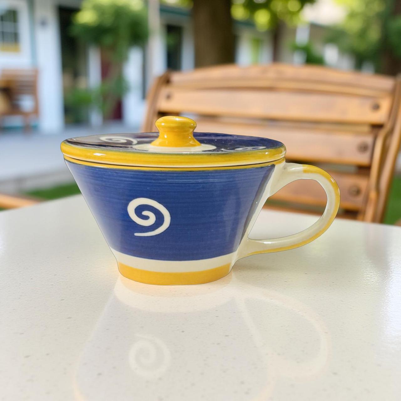Blue mug with yellow rim and handle on a white surface outdoors