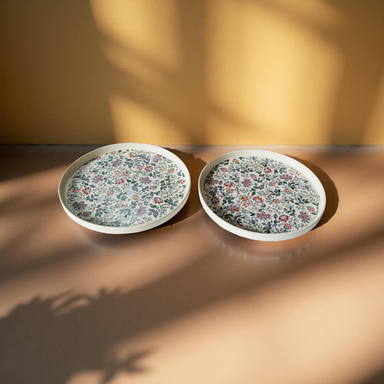 Two floral-patterned plates on a wooden surface with a warm light casting shadows.