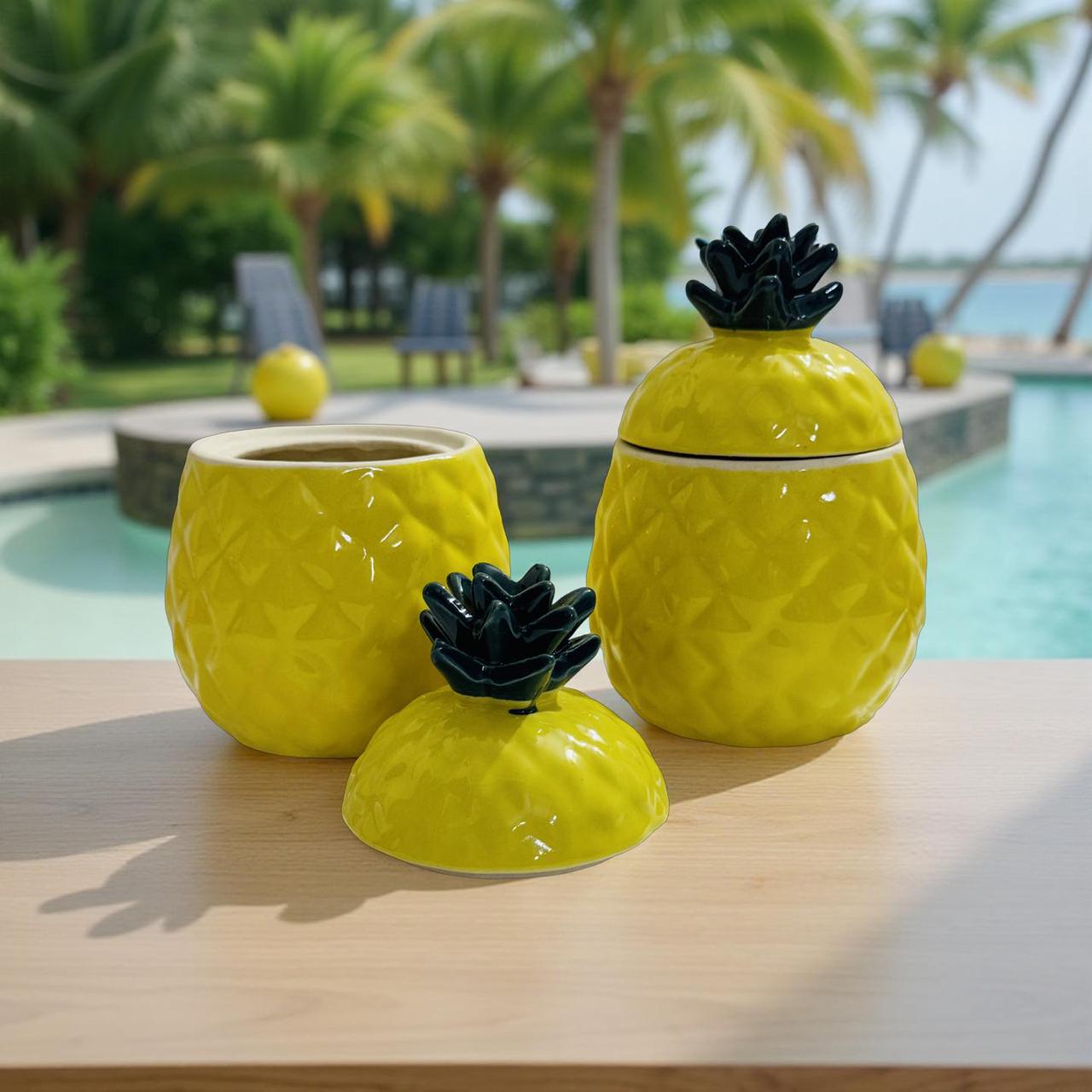 Three yellow pineapple-shaped ceramic jars with black lids on a wooden surface by a poolside.