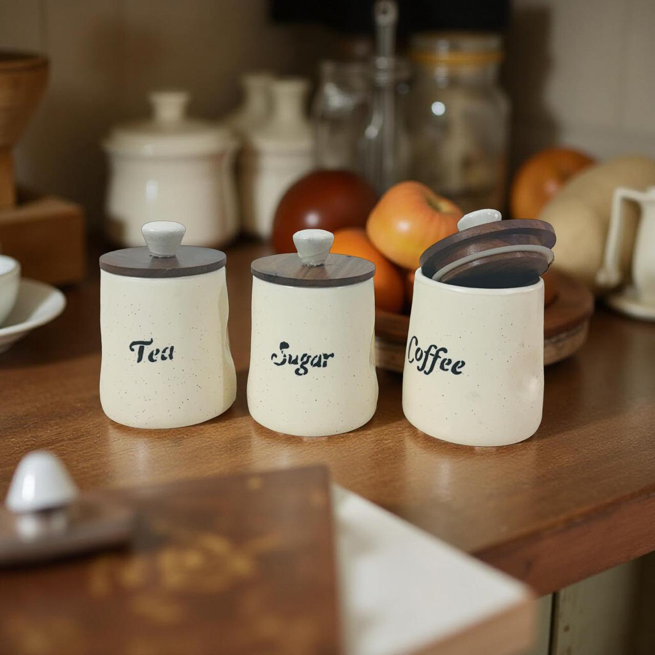 Three ceramic jars labeled 'Tea', 'Sugar', and 'Coffee' on a wooden surface with kitchen items in the background.