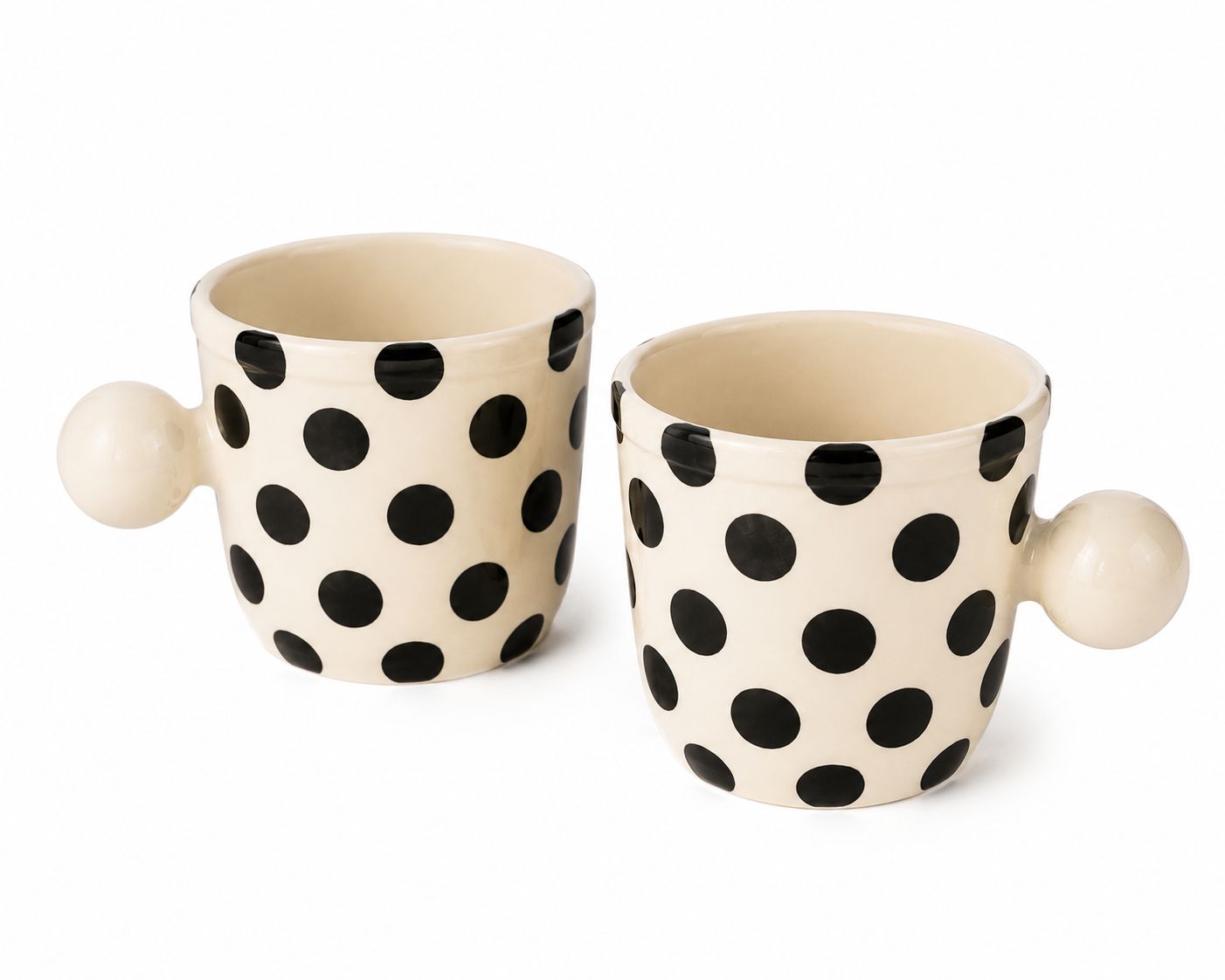Two cream-colored ceramic mugs with black polka dots and spherical side handles, shown on a clean white background.