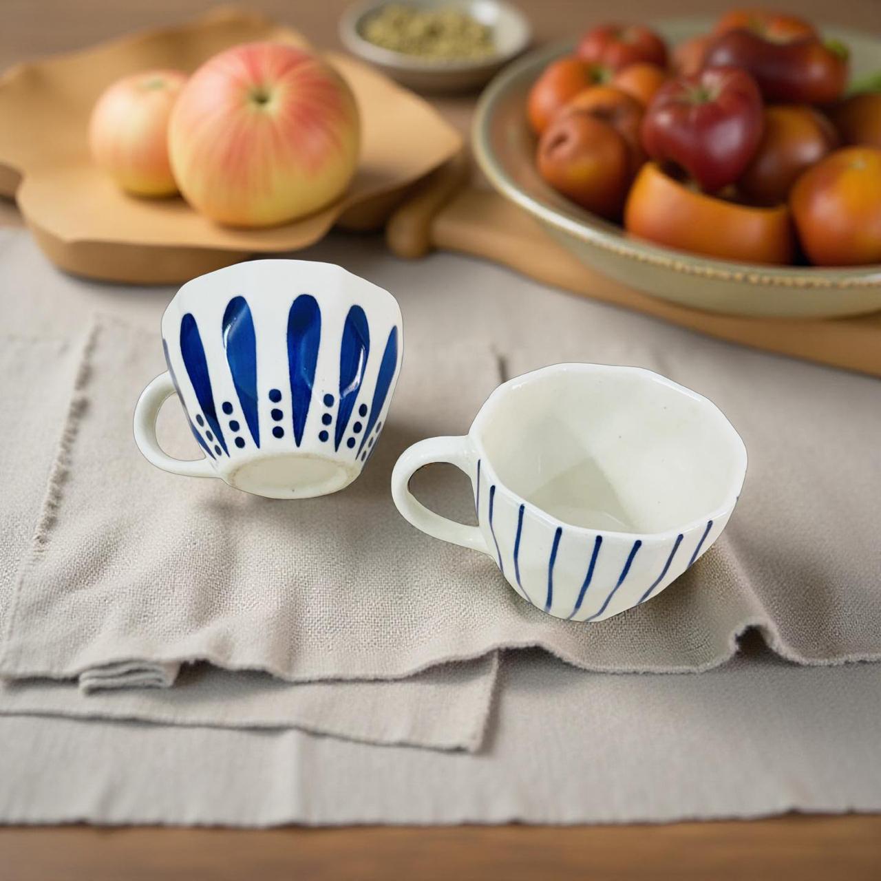 Two ceramic cups with blue patterns on a textured surface with apples in the background