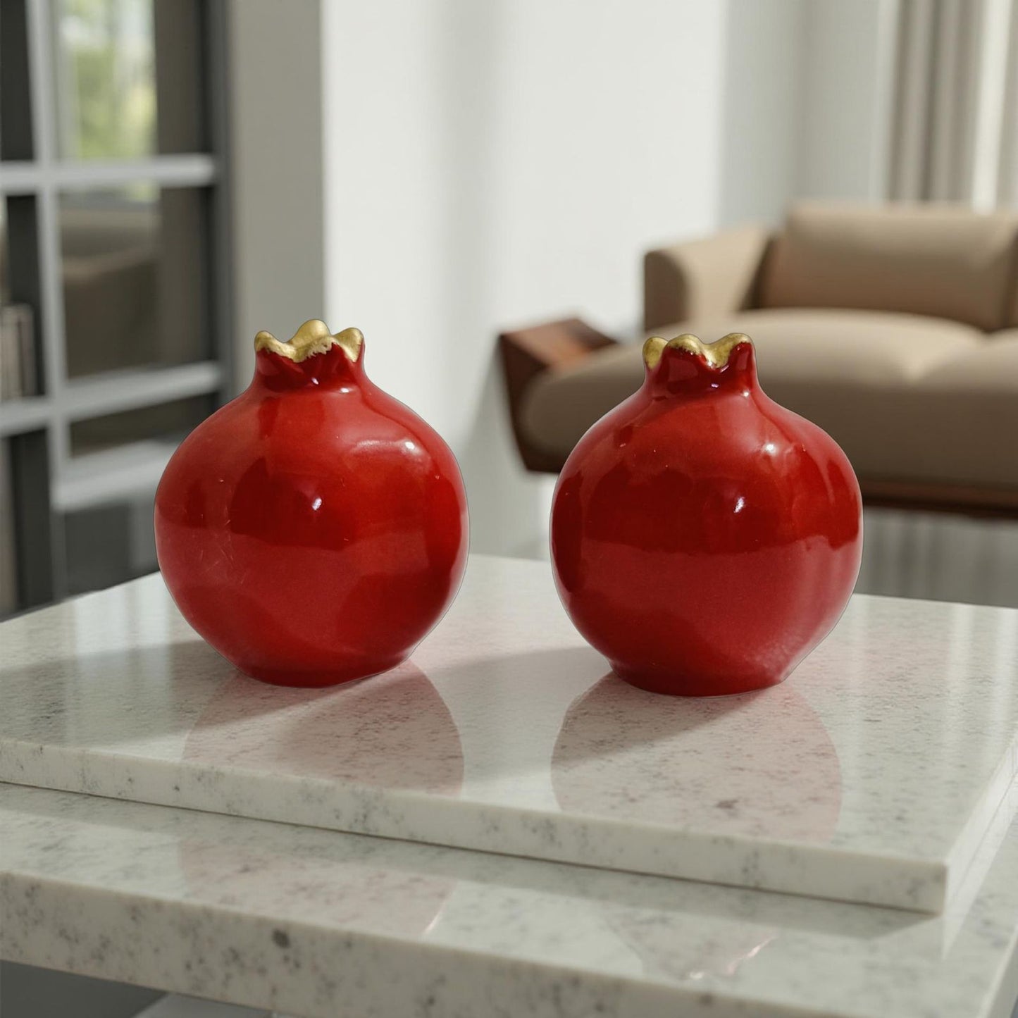 Two red ceramic pomegranate-shaped vases with gold accents on a marble surface.