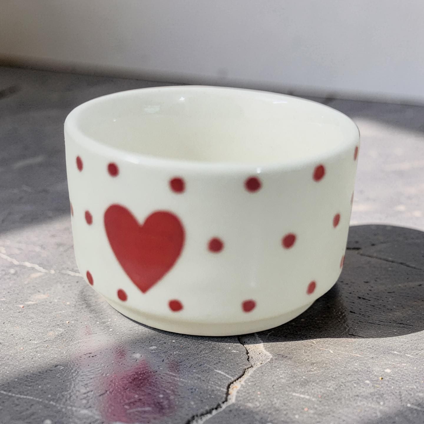 White ceramic cup with red heart and polka dot patterns on a stone surface.