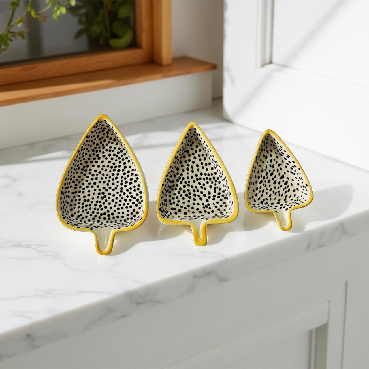 Three leaf-shaped ceramic bowls with black dot patterns on a marble surface.