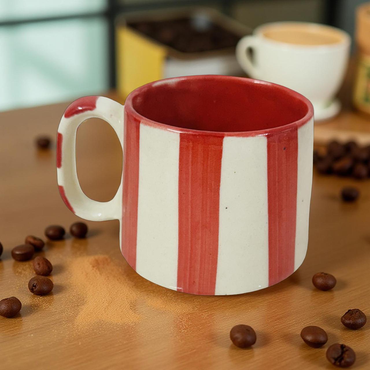 Red and white striped mug on a wooden surface with coffee beans and another cup in the background.