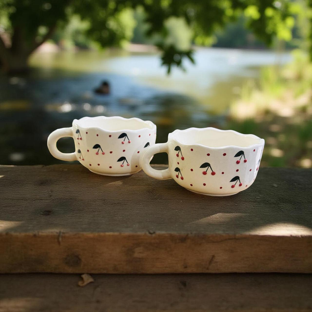 Two ceramic cups with cherry pattern on a wooden surface outdoors.