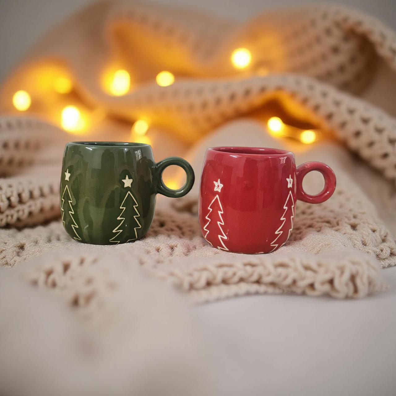 Two Christmas-themed mugs on a soft surface with warm lighting in the background.