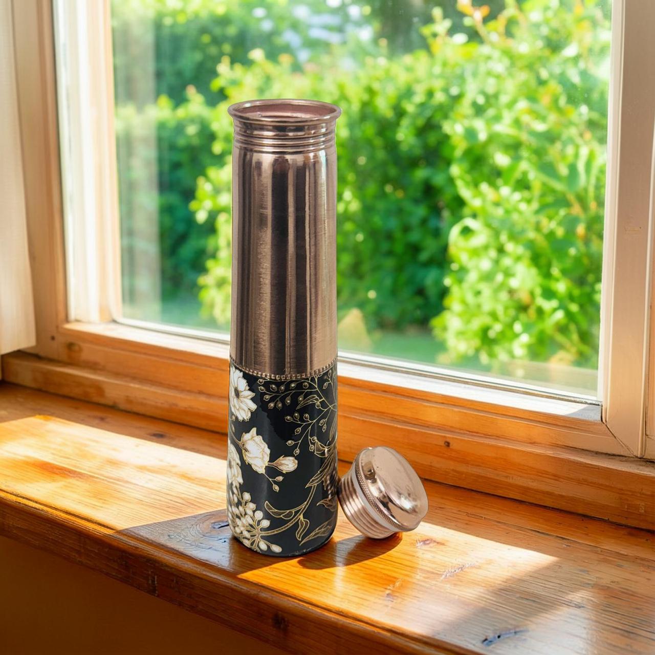 Decorative water bottle with floral design on a windowsill with greenery outside