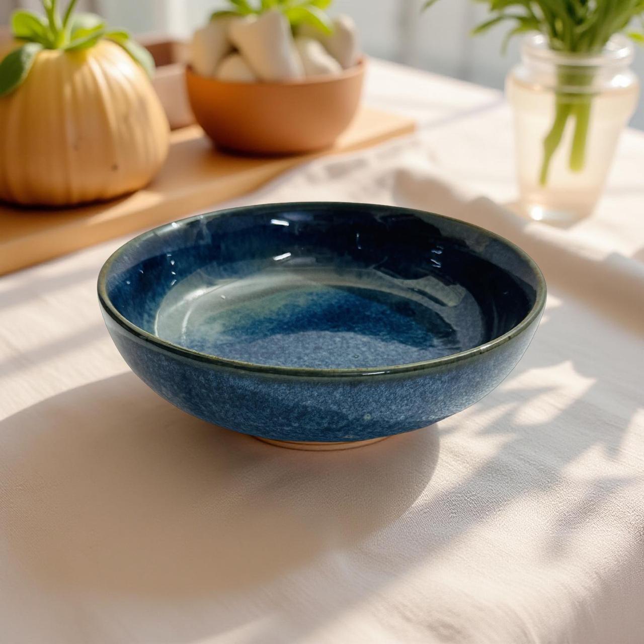 Blue ceramic bowl on a light surface with plants in the background