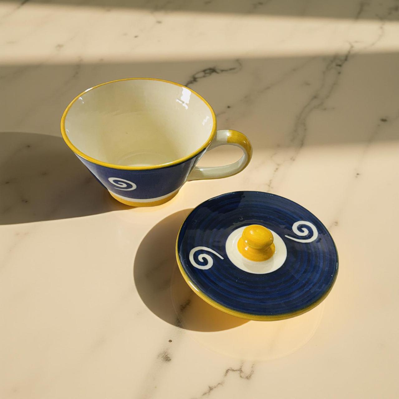 Ceramic cup and saucer with blue and yellow design on a marble surface