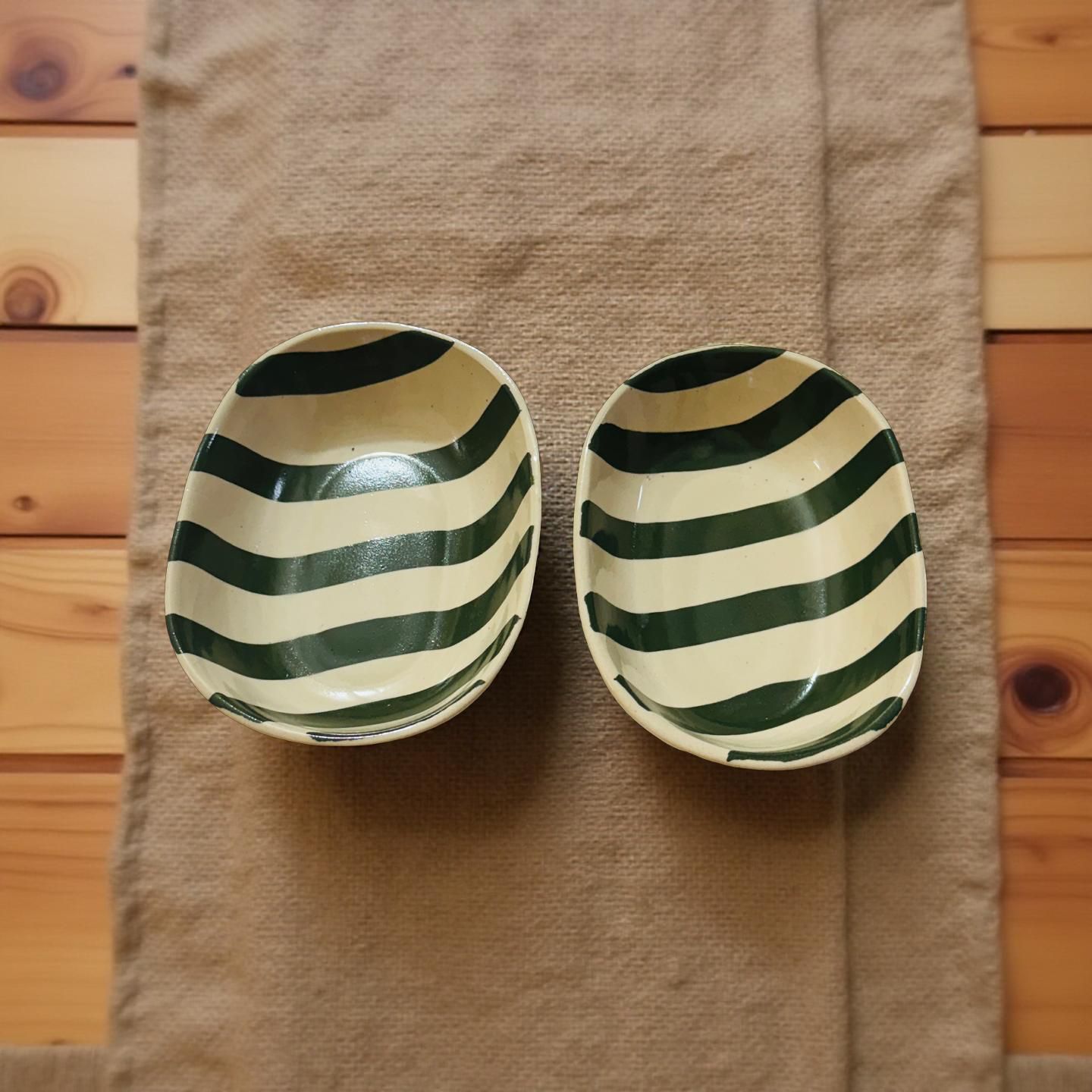 Two ceramic bowls with green and beige stripes on a textured fabric background.