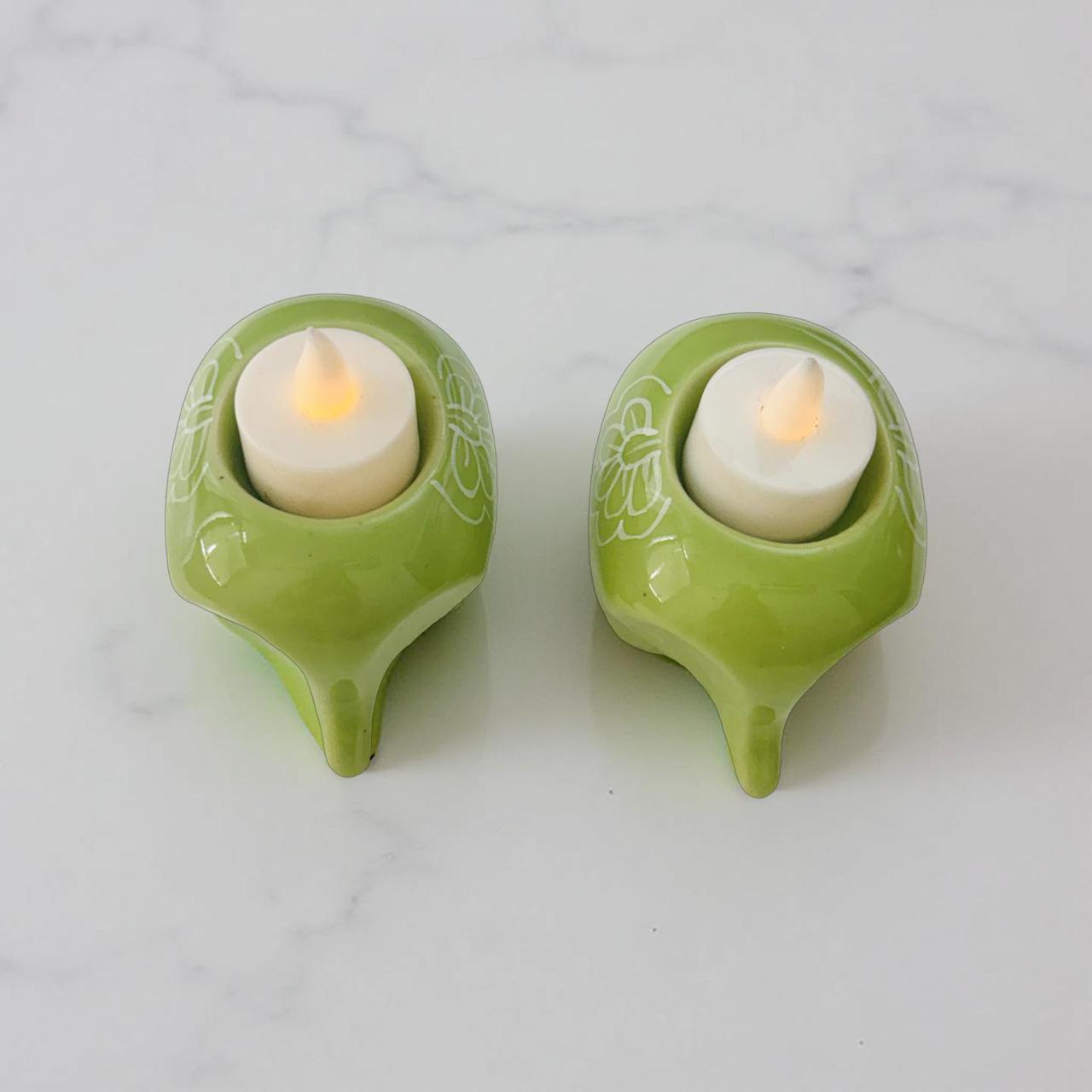 Two green candle holders with lit candles on a light gray background