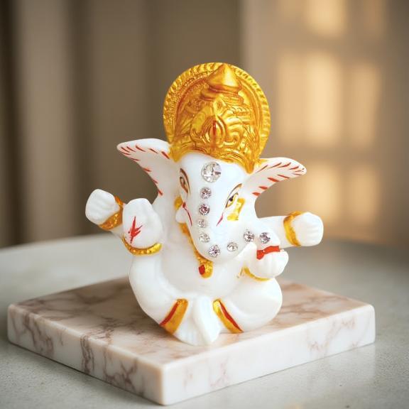 White and gold Ganesh statue on a marble base with a blurred background