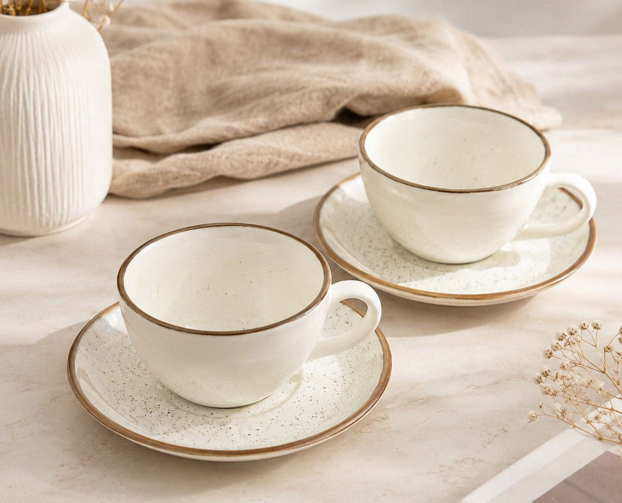Two ceramic tea cups with saucers on a light surface with a neutral background