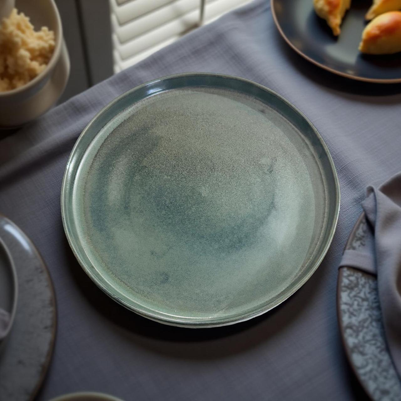 Green ceramic plate on a table with other dishes and food items.