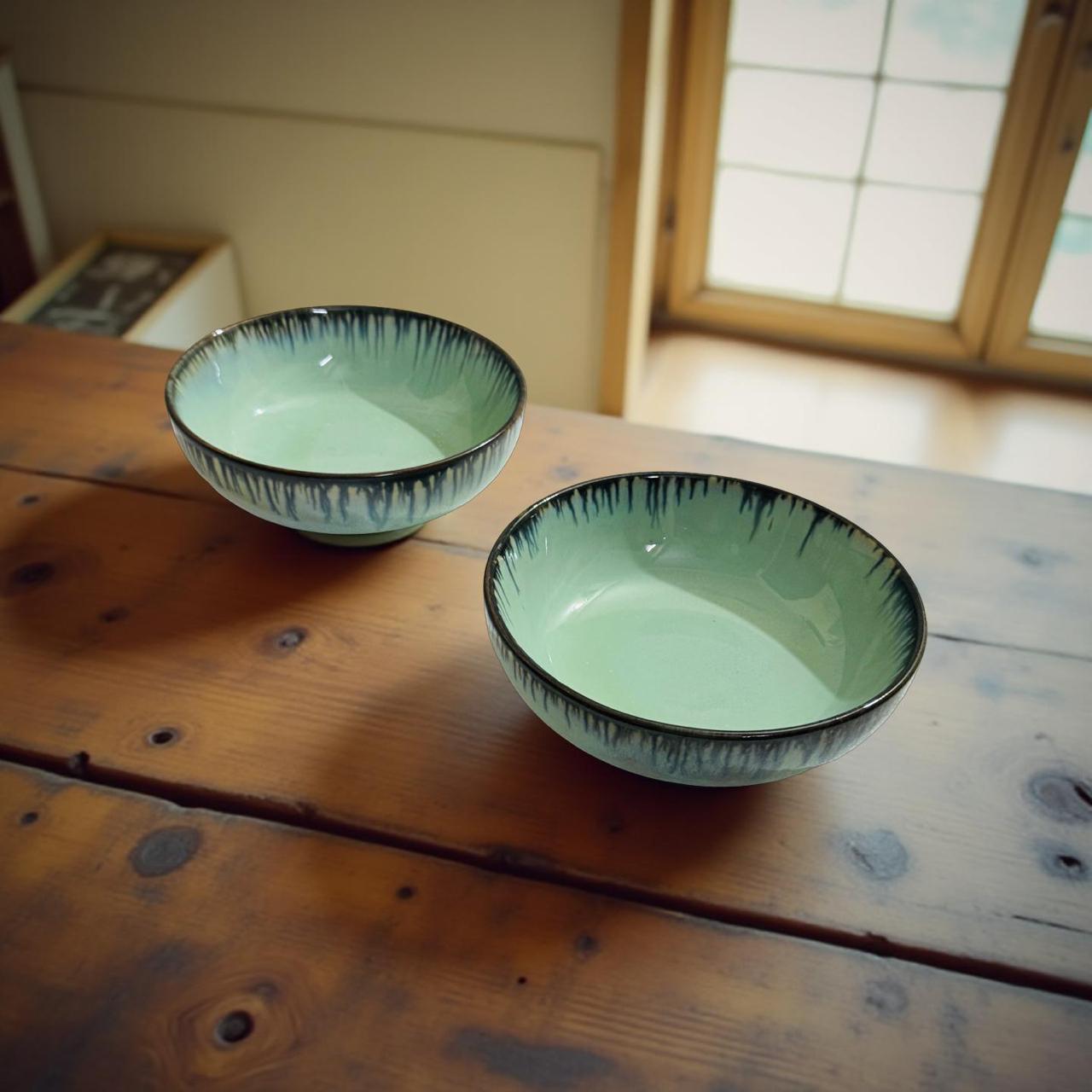 Two green ceramic bowls with black rims on a wooden surface.
