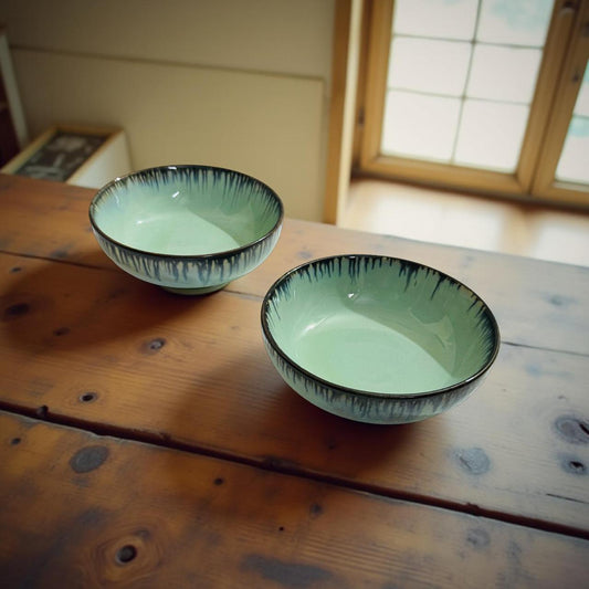 Two green ceramic bowls with black rims on a wooden surface.