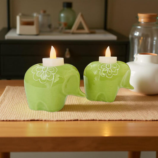 Two green elephant-shaped candle holders with candles on a wooden table.