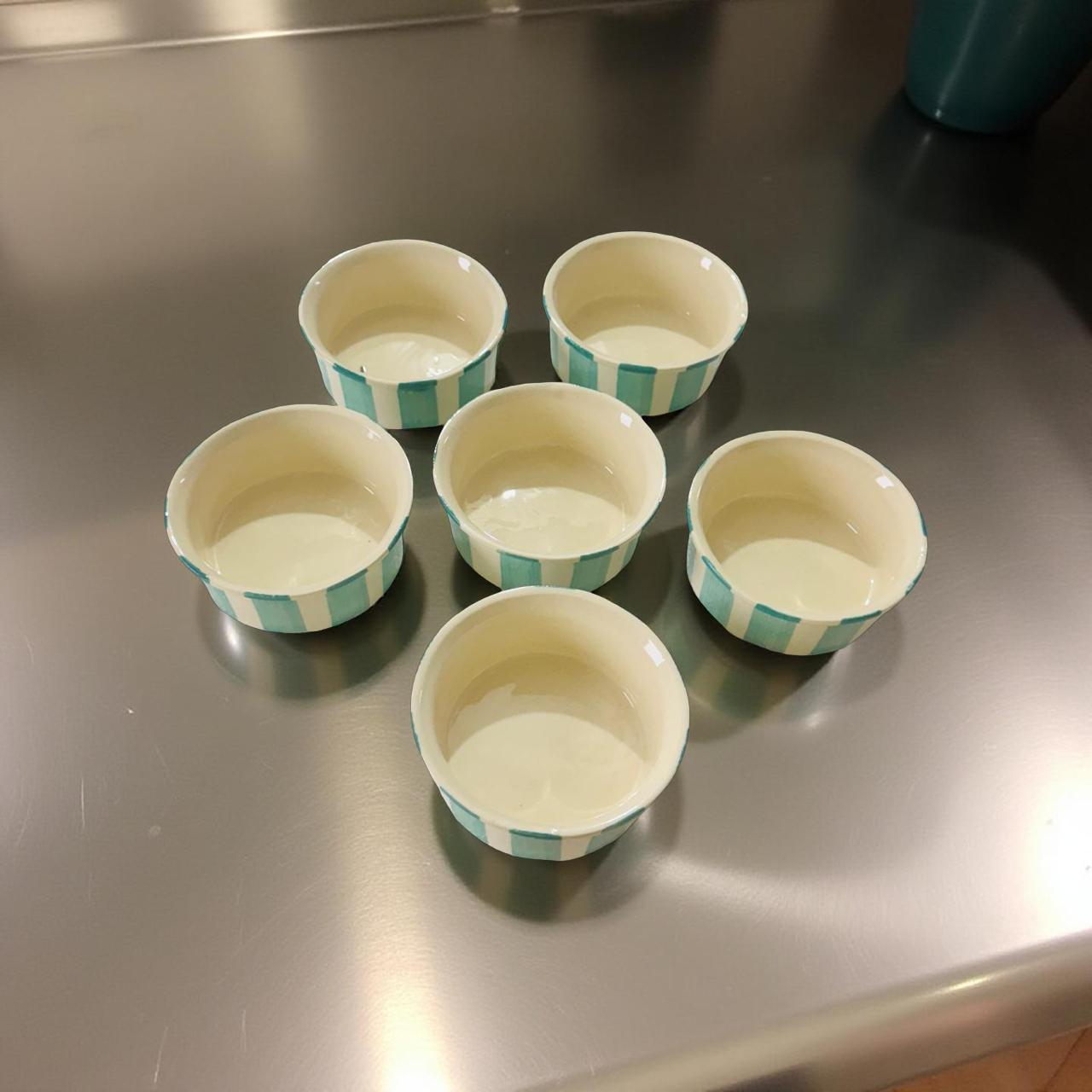 Set of six ceramic bowls with green checkered rim on a metallic surface
