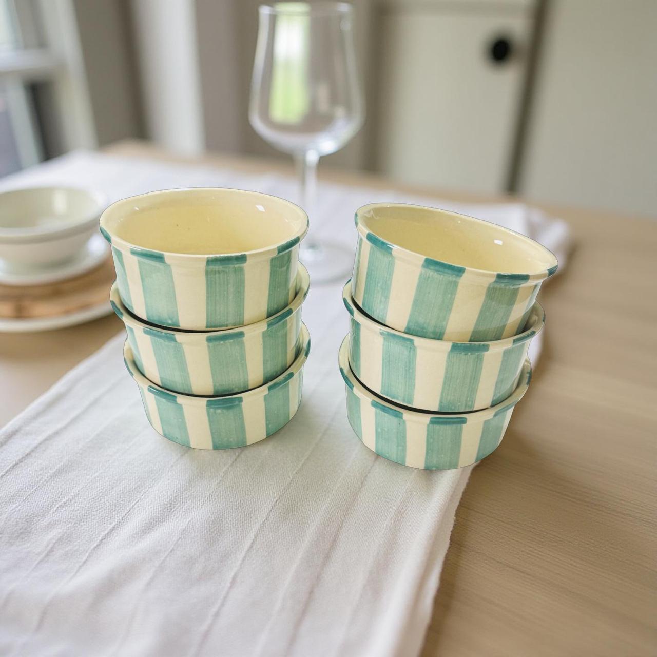 Set of striped ceramic bowls on a table with a glass in the background