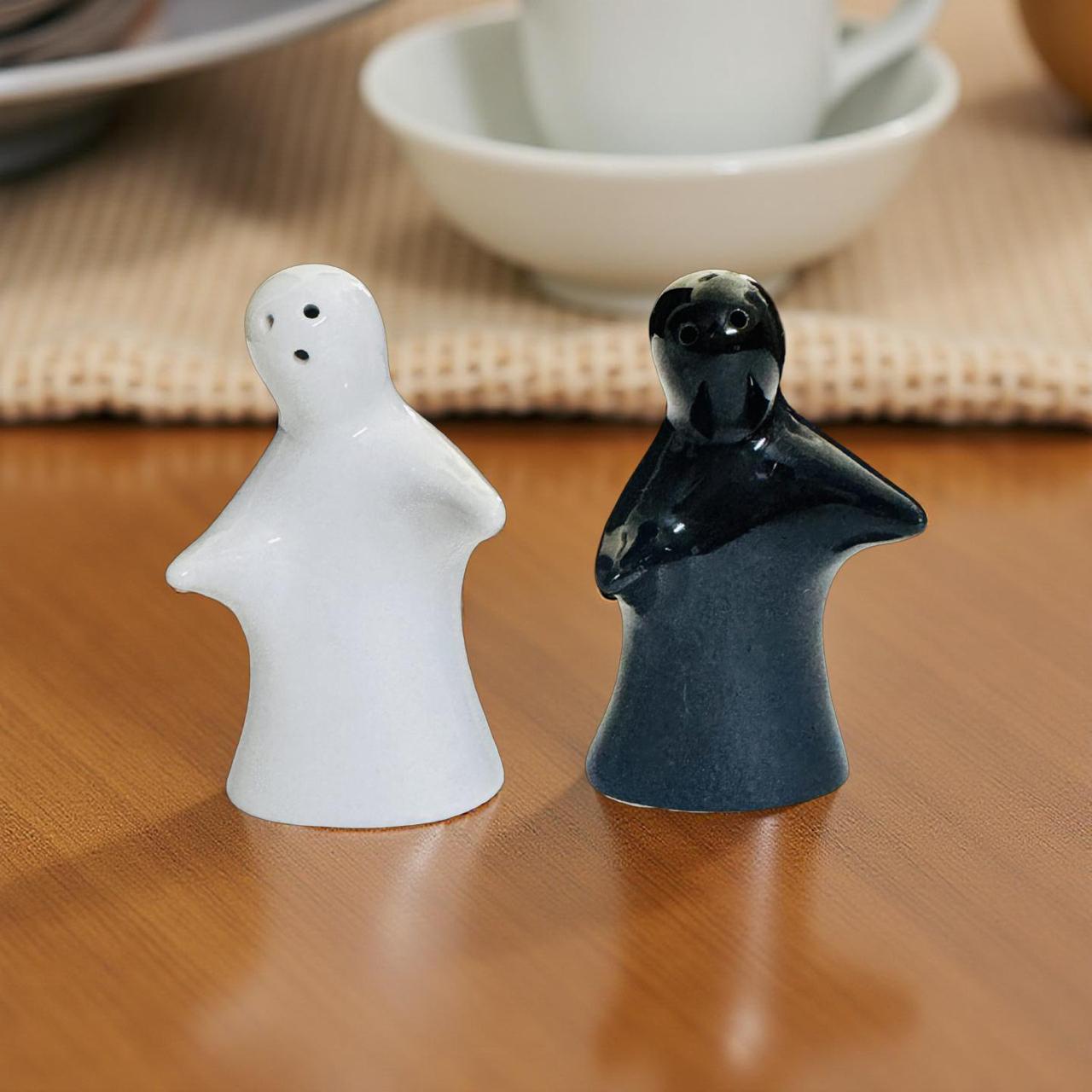 White and black ceramic salt and pepper shakers on a wooden surface with a blurred background.