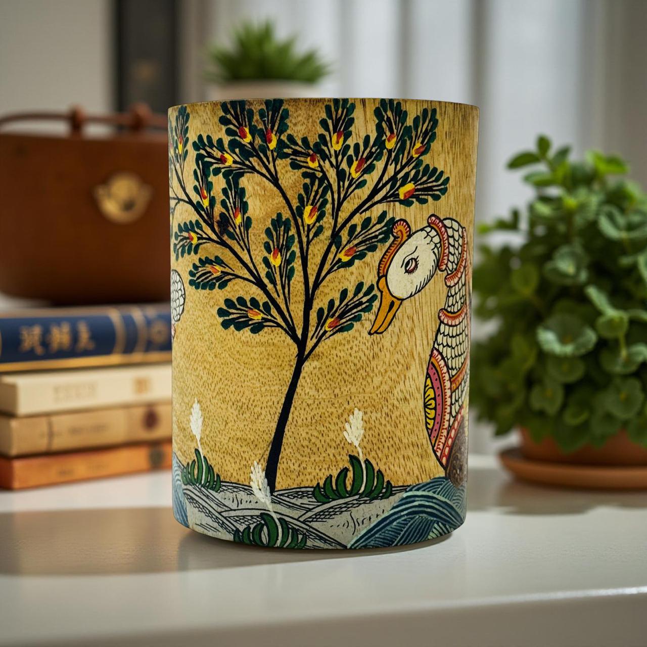 Decorative vase with artistic design of a tree and bird on a shelf with books and plants.