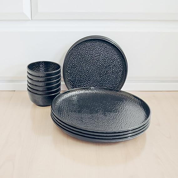 Set of black textured melamine plates and bowls on a light wooden surface.