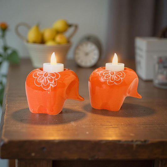 Two orange elephant-shaped candles with white floral designs on a wooden surface.