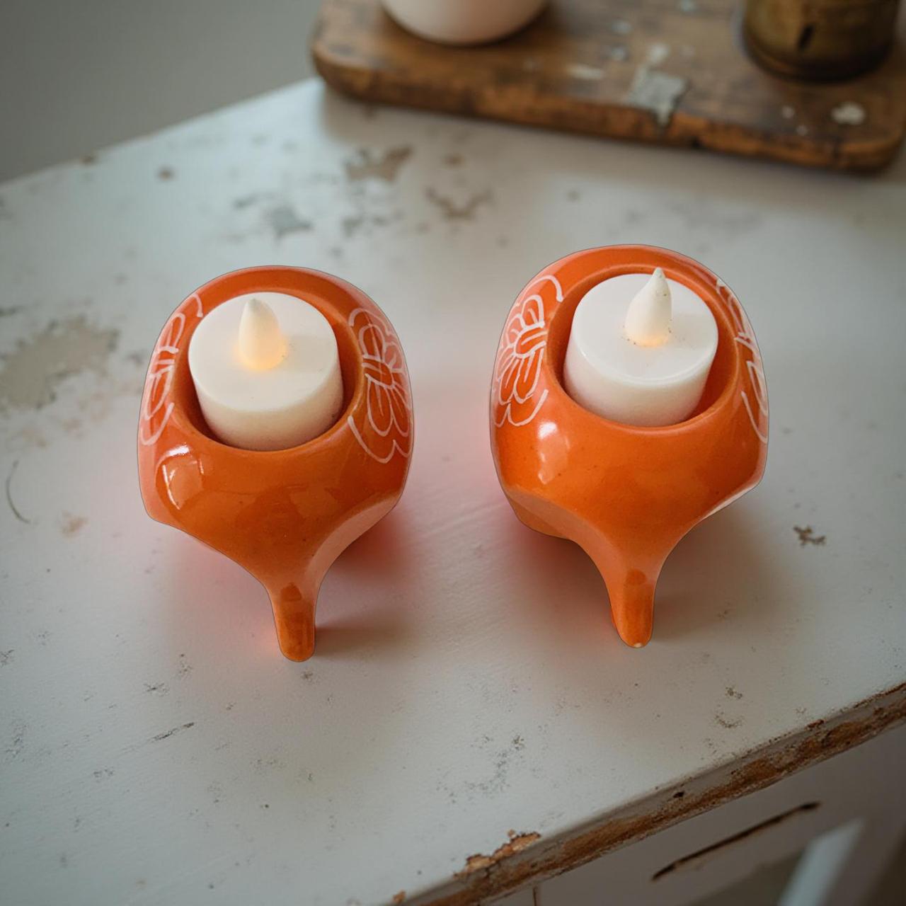 Two orange ceramic holders with white candles on a rustic surface.
